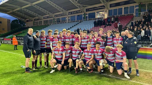 A rugby team poses together on the field, wearing striped jerseys, celebrating after a match.