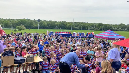 A large crowd of children in striped shirts gathers at a rugby festival with tents.